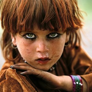 © REZA / Enfance à Tora Bora Afghanistan. Zones tribales. 2004 / Petite fille afghane, près de Tora Bora dans la zone tribale pashtoune, près de la frontière pakistanaise. « Et toi, elle est où ta maison ? Elle est là-haut, tout près du village. Je cours toute la journée. Je joue avec la terre. Je parle aux fleurs et je me cache derrière les arbres. Quand je vois un étranger, je cours vite, vite jusqu’à ma maison.  Et toi, elle est où ta maison ? Tu sais, un jour, je les ai vus de loin. Ils étaient comme les doigts de ma main. Ils marchaient tout doucement, comme s’ils voulaient se cacher. Mais moi, je les ai regardés longtemps. Ils étaient bizarrement habillés. Ça devait peser lourd, surtout avec leur casque sur la tête. Mais ce qui m’a le plus impressionnée, c’est leur fusil. Chacun en tenait un dans ses mains, et ils regardaient tous comme s’ils avaient peur, comme s’ils cherchaient quelque chose. Tu sais, je suis courageuse parce que je suis restée à les regarder. Je les ai même entendus parler ; mais je n’ai rien compris à leur langue. Les hommes de mon village sont venus, même le chef. Les soldats sont rentrés chez tout le monde, ils ont regardé partout. Tout le monde était en colère. Je n’ai pas compris pourquoi ; personne n’a compris pourquoi ils étaient venus et ce qu’ils faisaient chez nous. Dis, peut-être que tu sais toi… Et eux, elle est où leur maison ? »