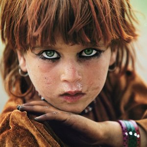 © REZA / Webistan I Enfance à Tora Bora Afghanistan I Zones tribales I 2004 I Petite fille afghane, près de Tora Bora dans la zone tribale pashtoune, près de la frontière pakistanaise. « Et toi, elle est où ta maison ? Elle est là-haut, tout près du village. Je cours toute la journée. Je joue avec la terre. Je parle aux fleurs et je me cache derrière les arbres. Quand je vois un étranger, je cours vite, vite jusqu’à ma maison.  Et toi, elle est où ta maison ? Tu sais, un jour, je les ai vus de loin. Ils étaient comme les doigts de ma main. Ils marchaient tout doucement, comme s’ils voulaient se cacher. Mais moi, je les ai regardés longtemps. Ils étaient bizarrement habillés. Ça devait peser lourd, surtout avec leur casque sur la tête. Mais ce qui m’a le plus impressionnée, c’est leur fusil. Chacun en tenait un dans ses mains, et ils regardaient tous comme s’ils avaient peur, comme s’ils cherchaient quelque chose. Tu sais, je suis courageuse parce que je suis restée à les regarder. Je les ai même entendus parler ; mais je n’ai rien compris à leur langue. Les hommes de mon village sont venus, même le chef. Les soldats sont rentrés chez tout le monde, ils ont regardé partout. Tout le monde était en colère. Je n’ai pas compris pourquoi ; personne n’a compris pourquoi ils étaient venus et ce qu’ils faisaient chez nous. Dis, peut-être que tu sais toi… Et eux, elle est où leur maison ? »